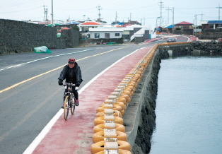 A person riding a bicycle alone on the bicycle path between the river and the road
